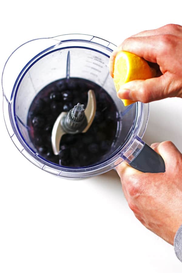 Blueberries and water in blender and squeezing a lemon over the blender