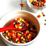 Candy Corn Snack Mix in a bowl with a red spoon scooping it out.