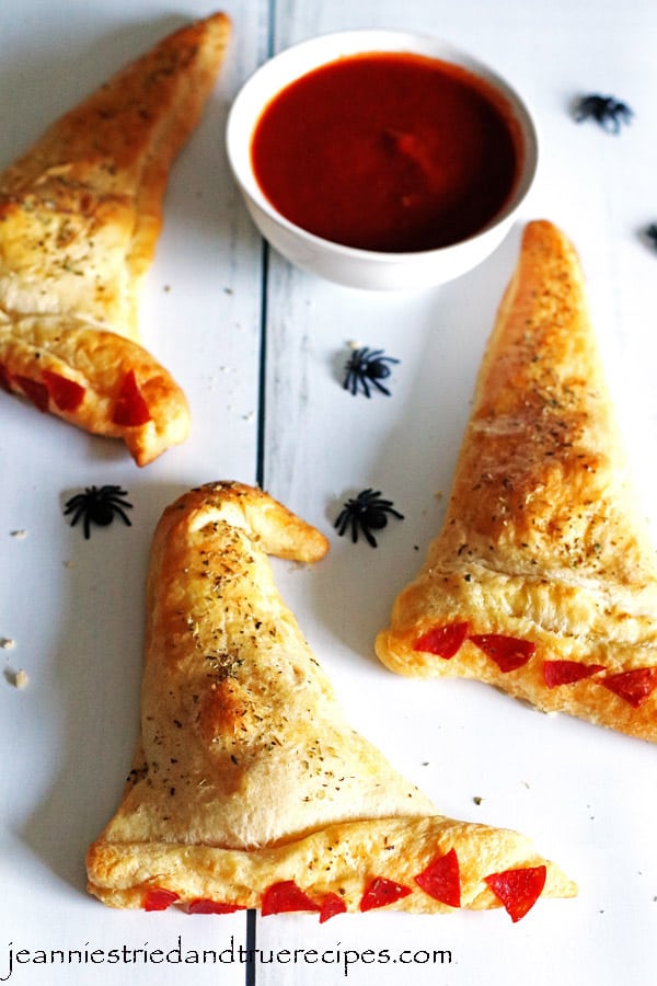 Witch Hat Calzones on a white table. There is a small white bowl with marinara sauce for dipping.