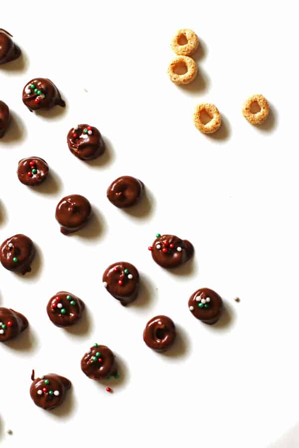Chocolate covered Cheerios with red and green sprinkles on white parchment paper