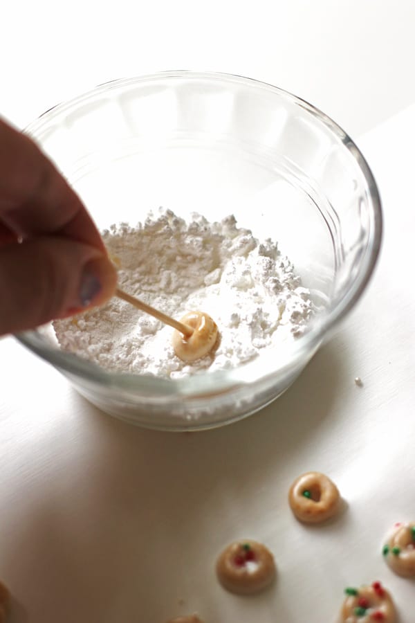 Dipping a Cheerio into powdered sugar in a small bowl
