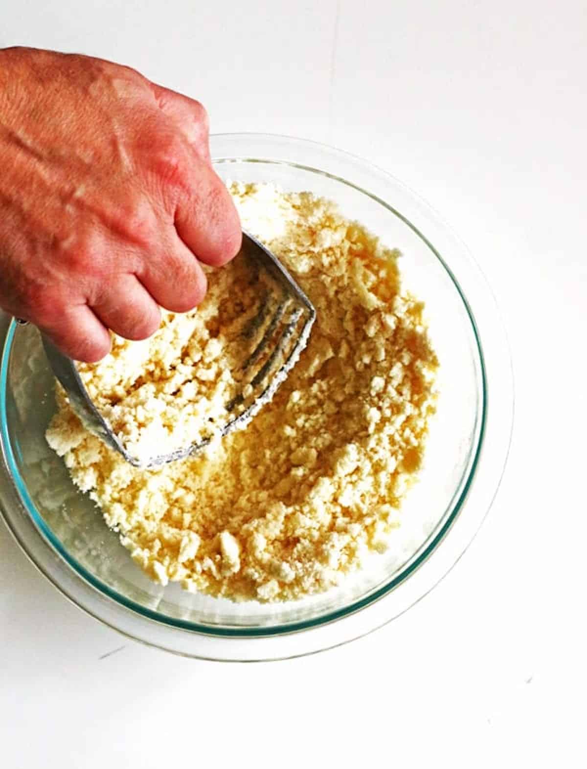 Making crumb topping for an apple pie by using a pastry blender to combine flour, sugar and softened butter