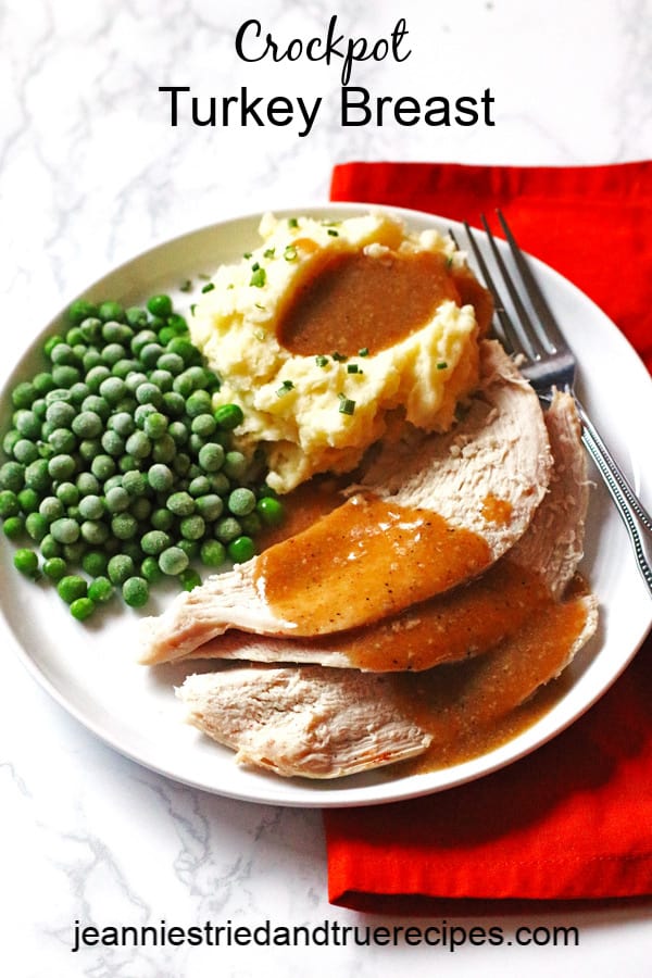 Turkey, homemade gravy, mashed potatoes and peas on a white plate with a fork