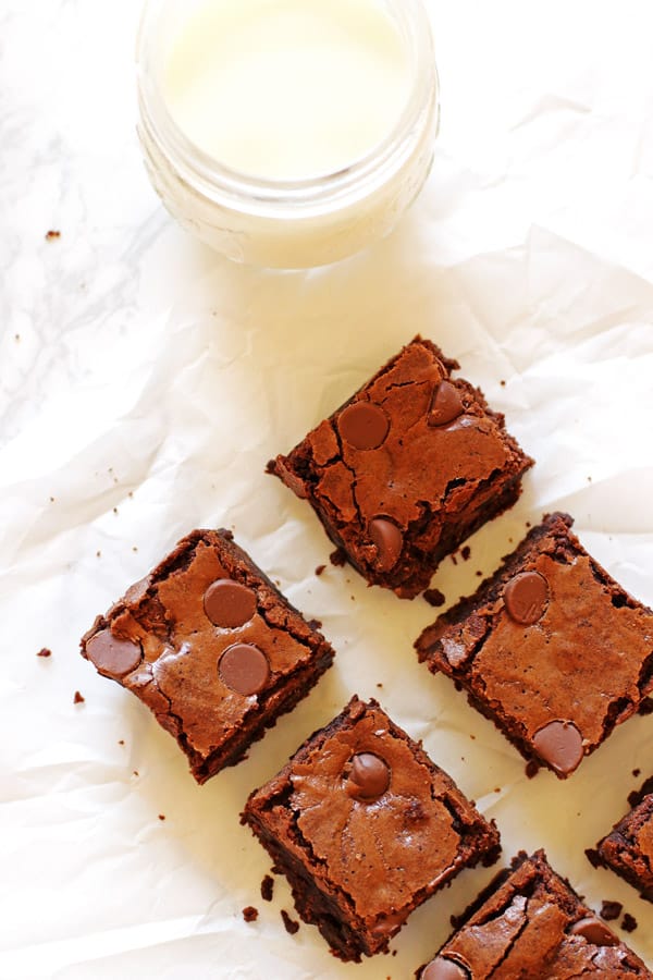 Brownies cut into squares on white parchment paper with a milk jug filled with milk
