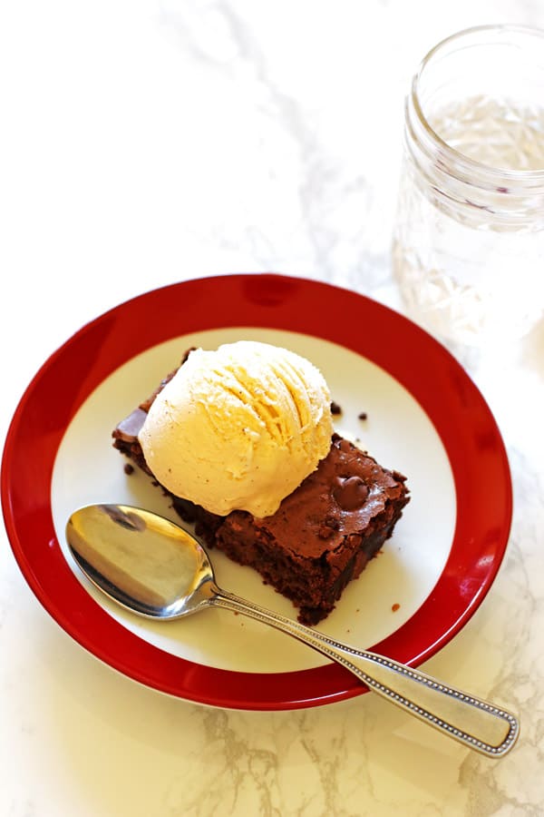 Brownie on a red and white plate with a scoop of vanilla ice cream on top of the brownie