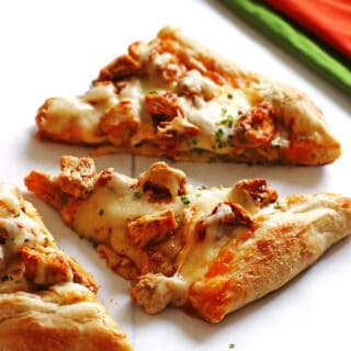 Pizza slices covered with cheese, chicken and chicken wing sauce on a white table.