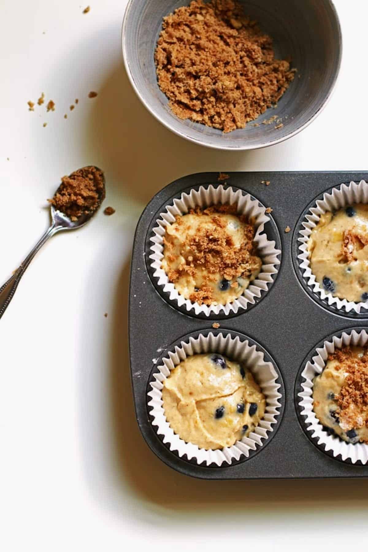 Muffin batter in lined muffin cups with brown sugar topping sprinkled over them