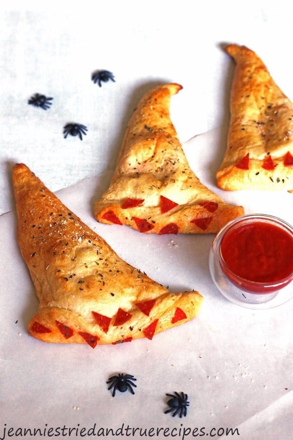 Witch Hat Calzones on a white table with a small bowl of marinara sauce. There are some plastic black spiders on the table for decoration.