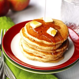 A stack of apple pancakes on a plate with slices of butter and maple syrup on them.