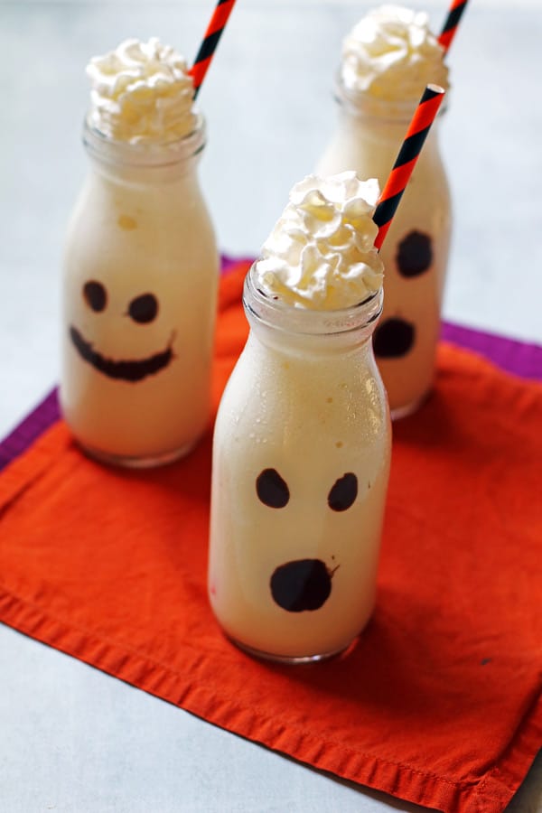 Milkshakes that are in a clear glass with faces on the glasses made out of melted chocolate.