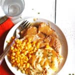Sliced turkey with gravy, mashed potatoes and corn on a white plate with a fork