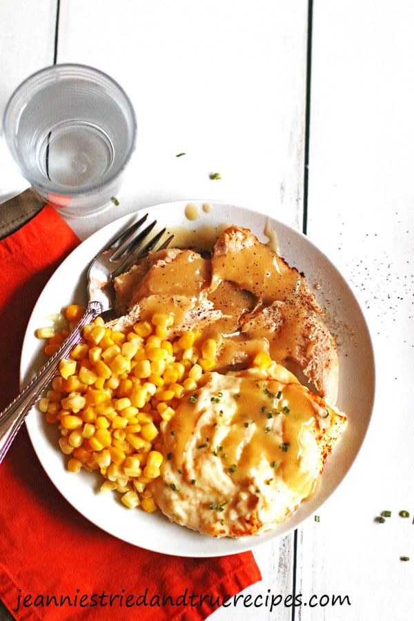 Sliced turkey with gravy, mashed potatoes and corn on a white plate with a fork