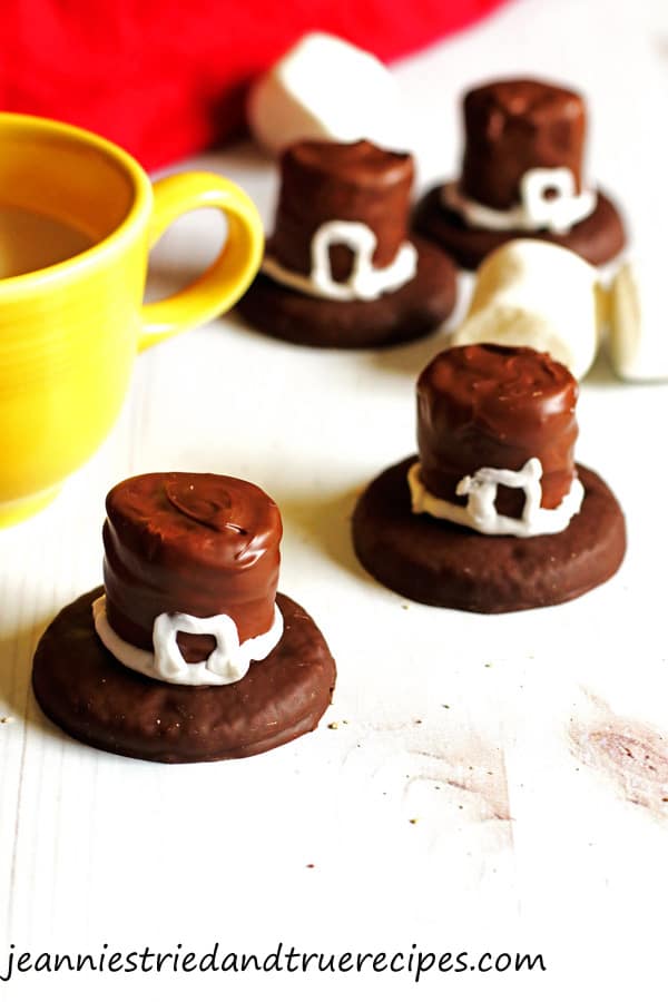 Cookies that are decorated as Pilgrim Hats sitting on a white table with a glass of milk