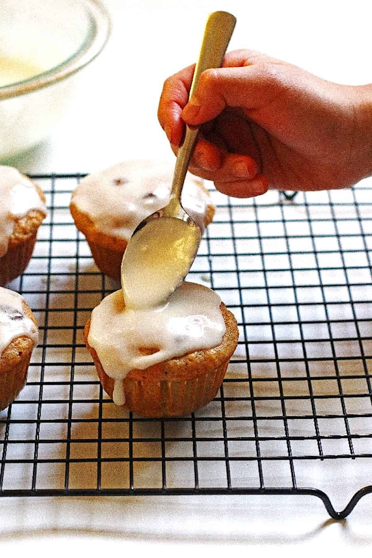 Using the back of a spoon to spread the glaze around on a muffin