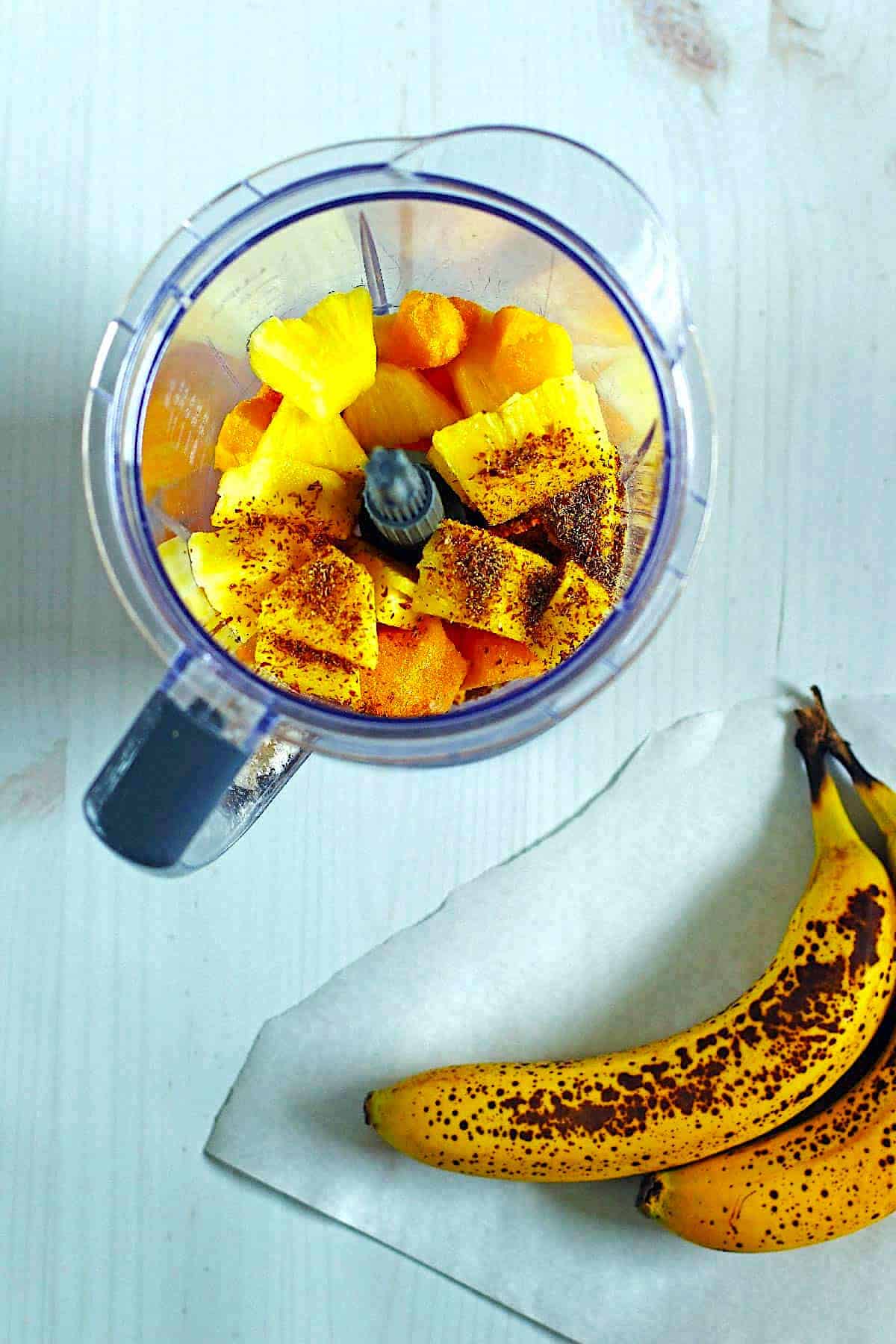 Smoothie ingredients in a blender and bananas next to the blender