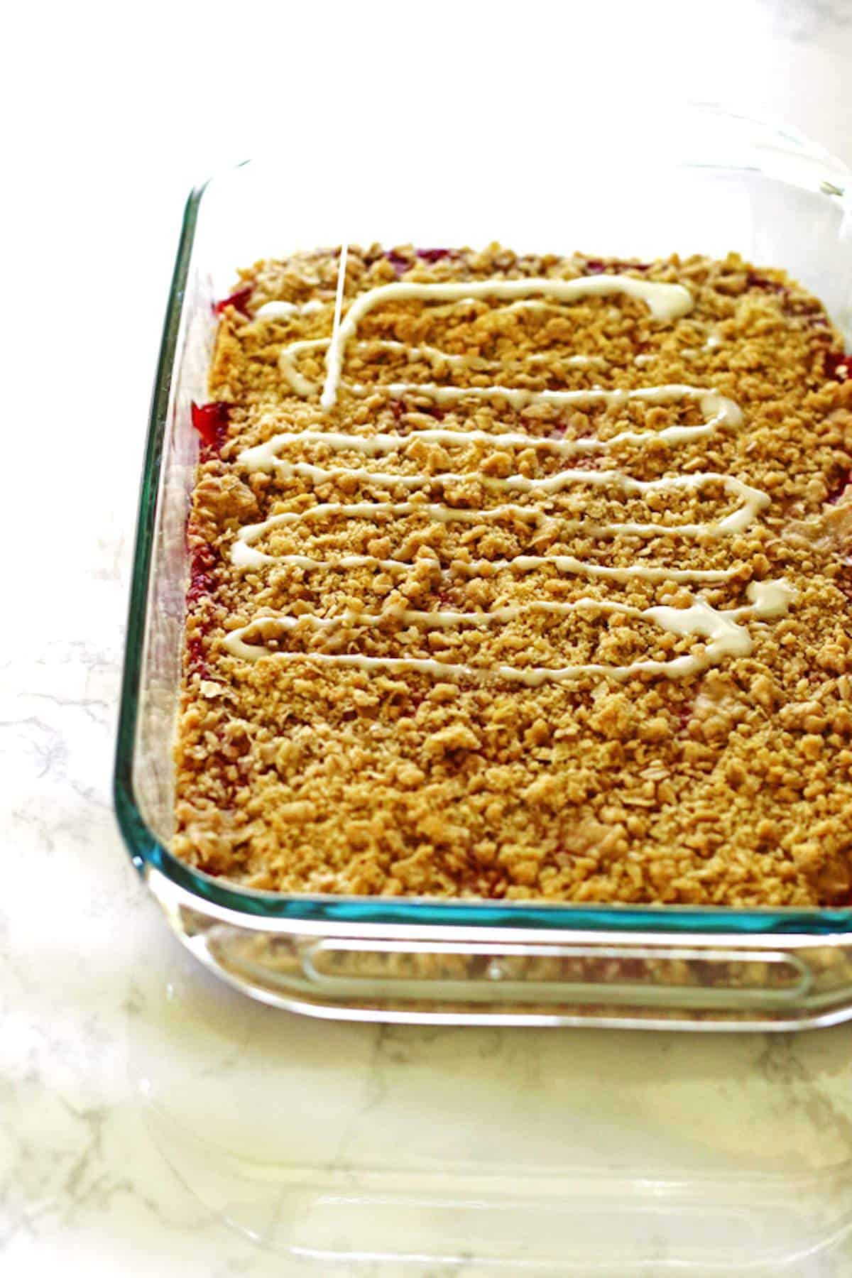 A pan of strawberry rhubarb bars with crumble topping and a sweet glaze on top.
