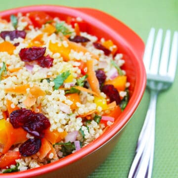 Vegetable quinoa salad with carrots and cranberries on a red plate.