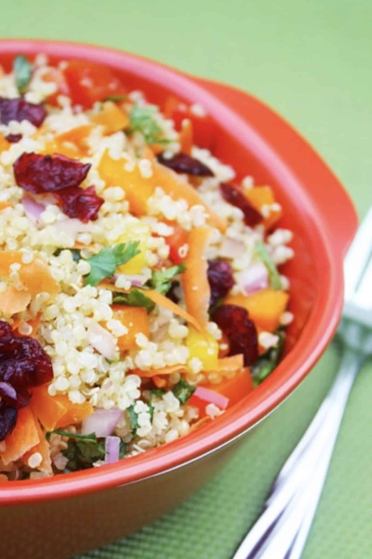 Vegetable quinoa salad with carrots and cranberries in a red bowl.