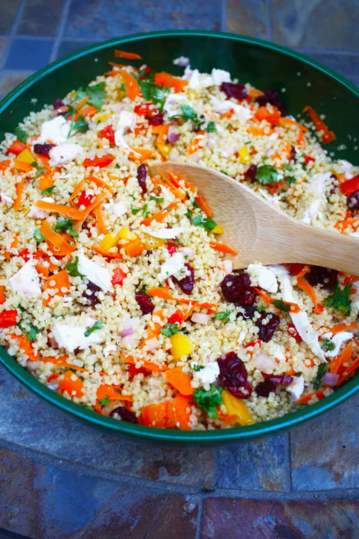 A green bowl filled with vegetable and chicken quinoa salad.