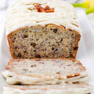 A cross section of a loaf of buttermilk banana bread with cream cheese frosting drizzled on the top.