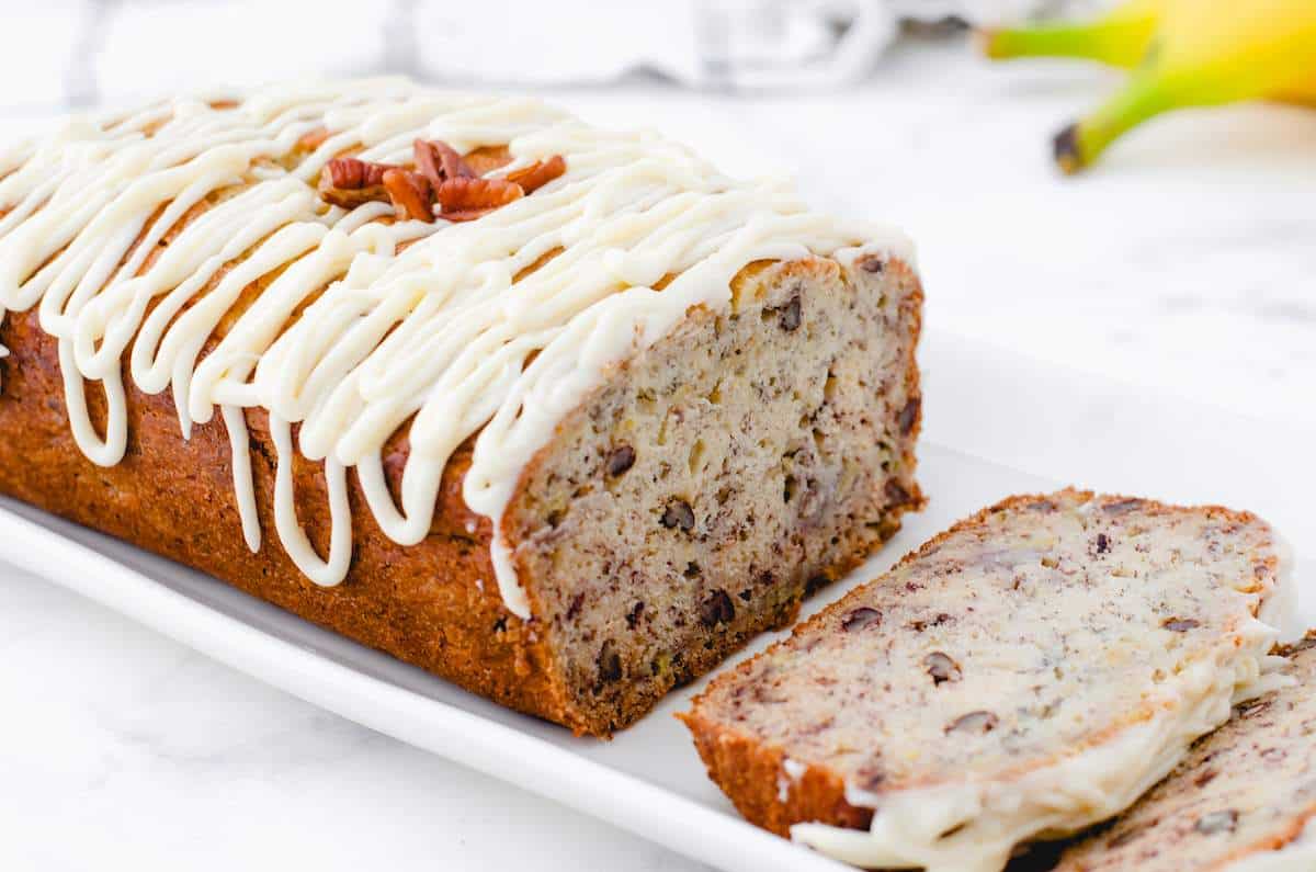 A loaf of sliced buttermilk banana bread with nuts with frosting drizzled on the top.