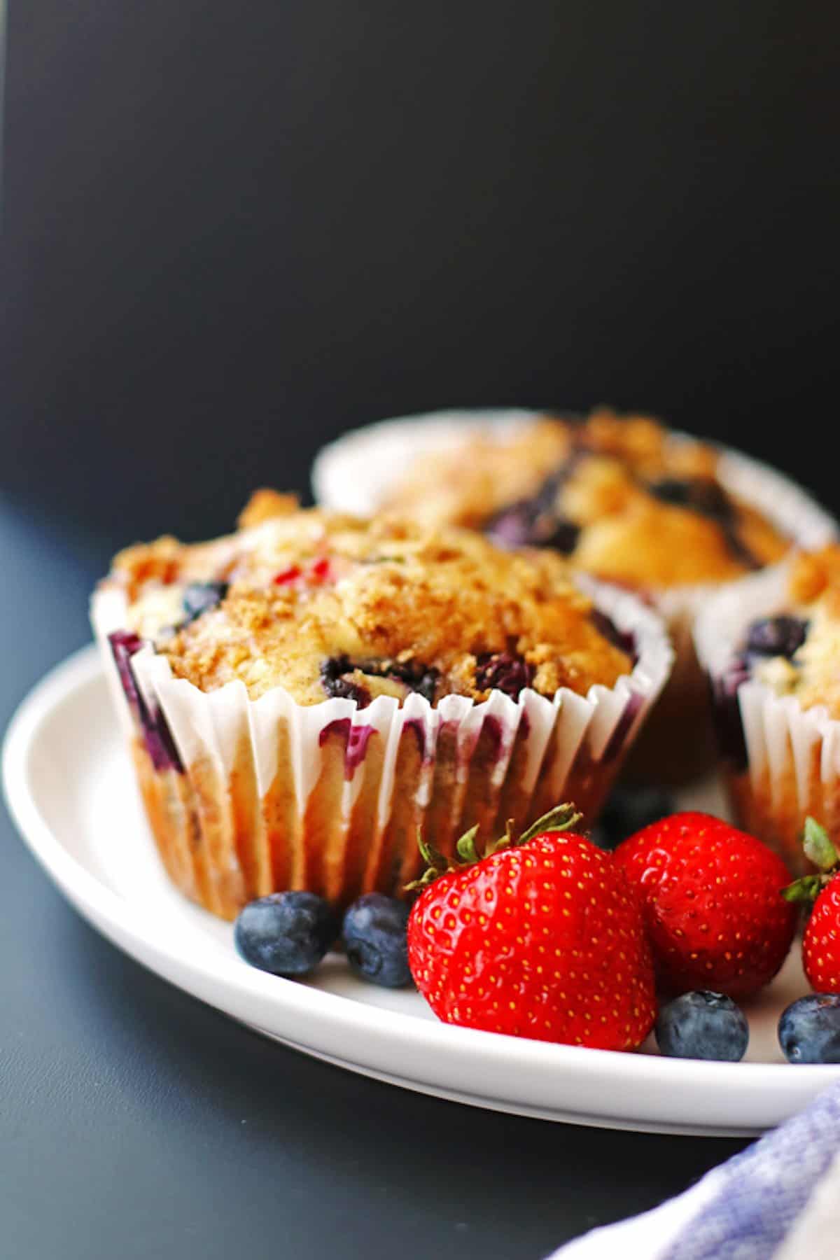 Three mixed berry muffins on a plate with berries.