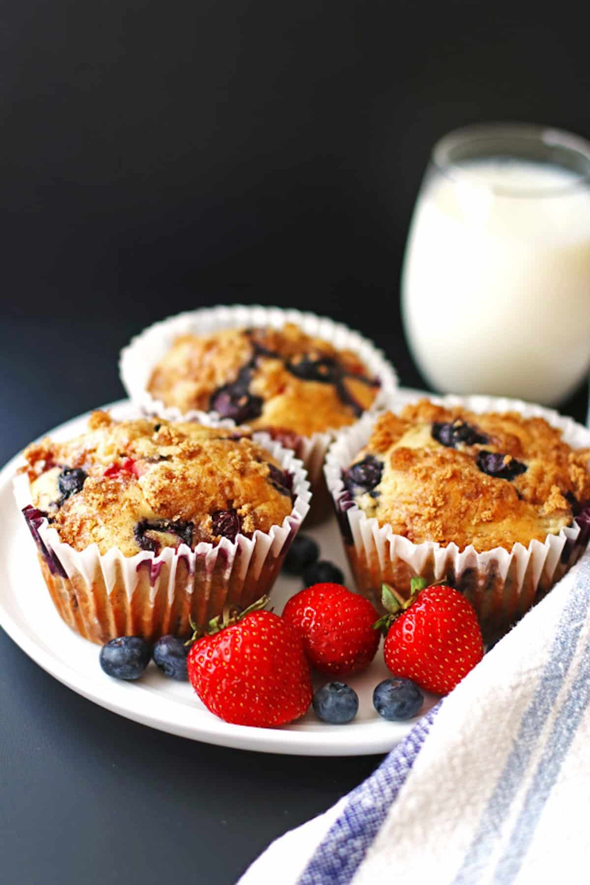 Three fruit explosion jumbo muffins on a plate with strawberries and blueberries.