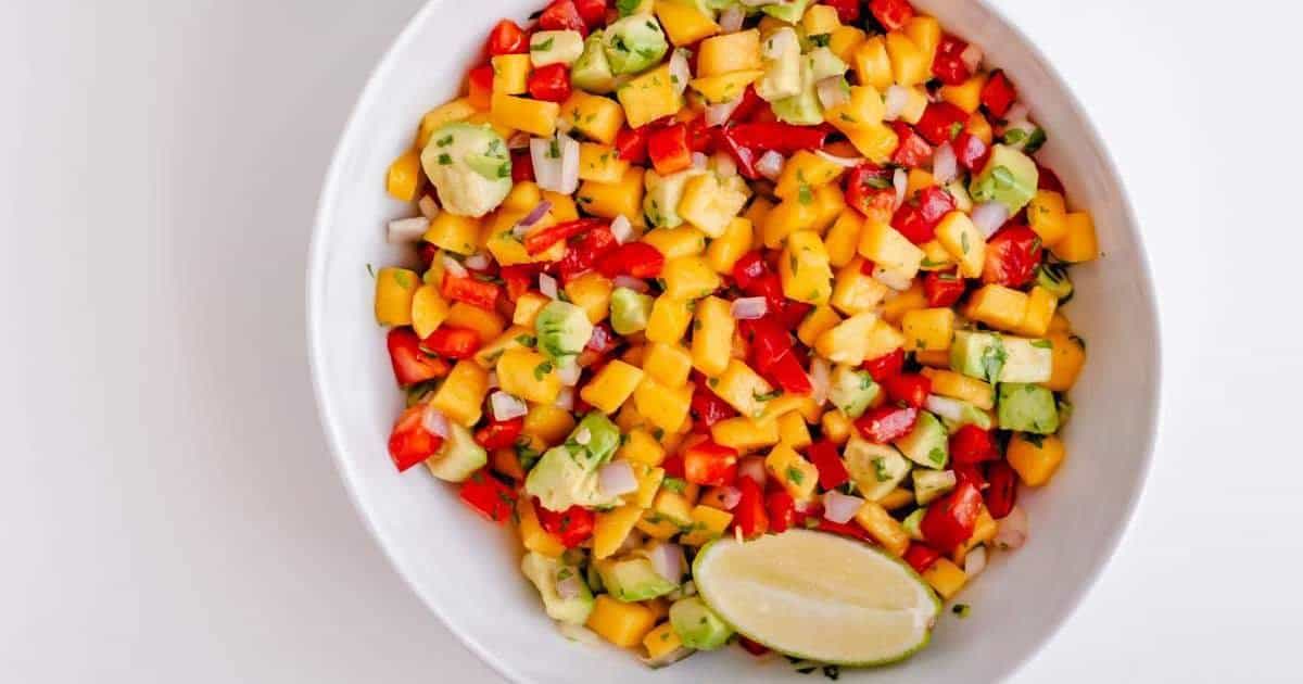 A bowl of mango and avocado salsa with a lime wedge.