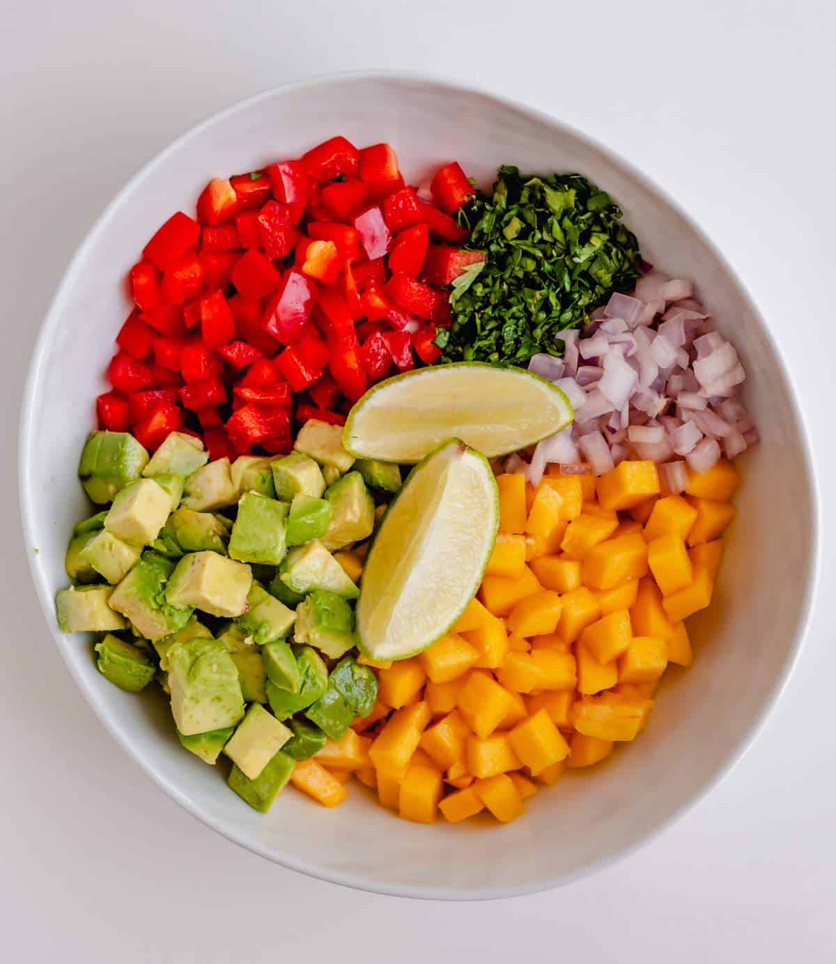 Make mango avocado salsa ingredients in a bowl - diced avocado, bell pepper, mango, onion, cilantro, and lime wedges