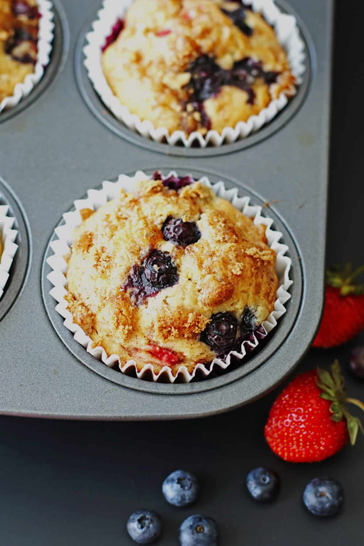 A mixed berry muffin in a paper liner in a muffin tin.