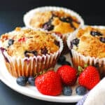 Three triple berry banana muffins on a plate with fresh berries.
