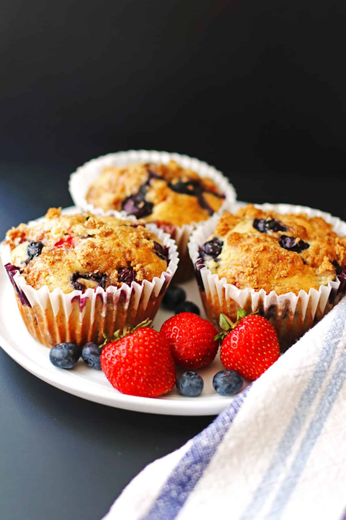 Three mixed berry muffins in paper liners on a plate.
