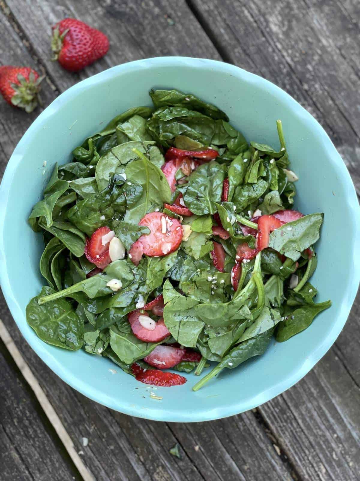 A blue bowl of strawberry and spinach salad with almonds, tossed with sesame poppyseed dressing.