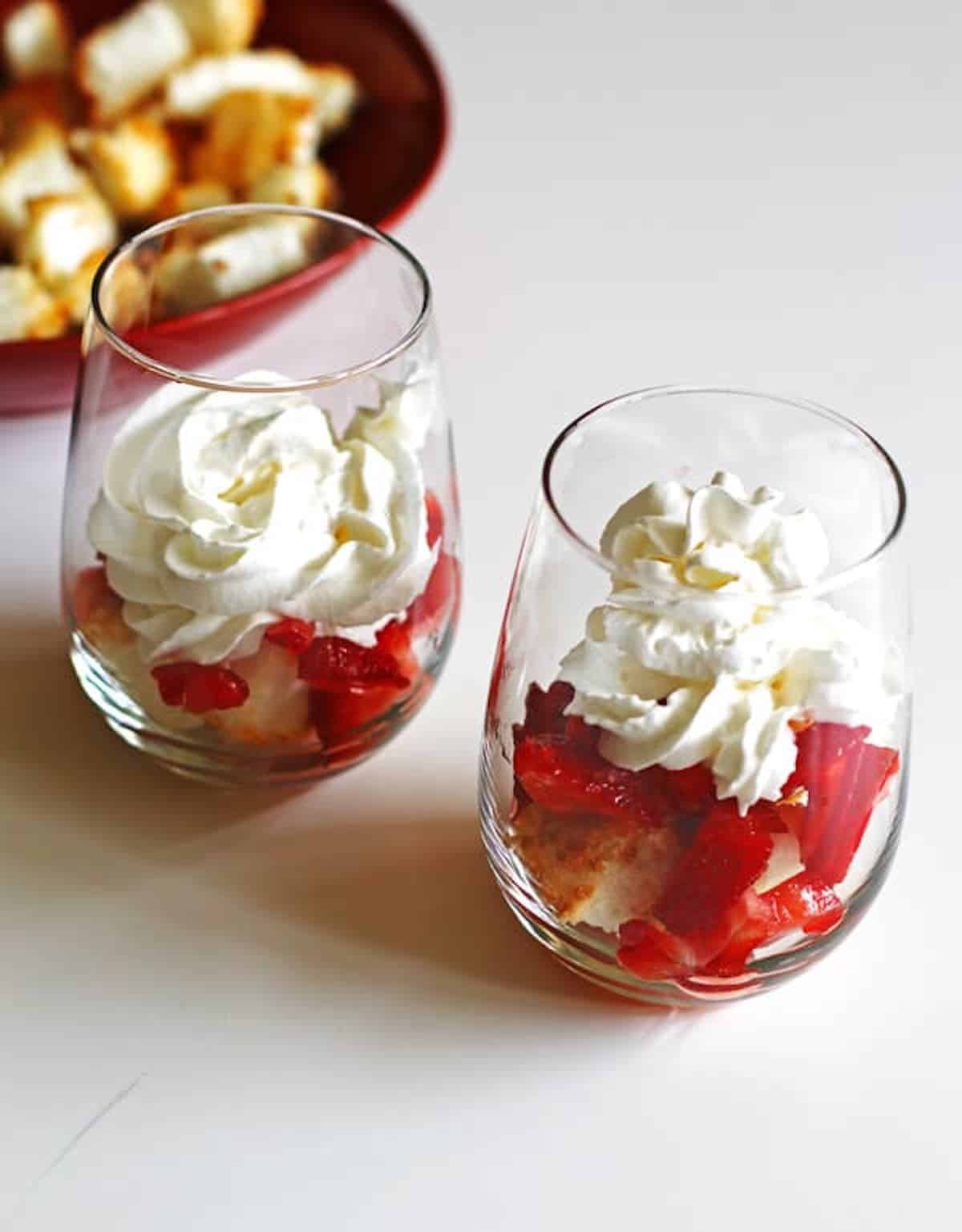 Toasted angel food cake cubes topped with strawberries and whipped cream in a wine glasses to assemble strawberry shortcakes.