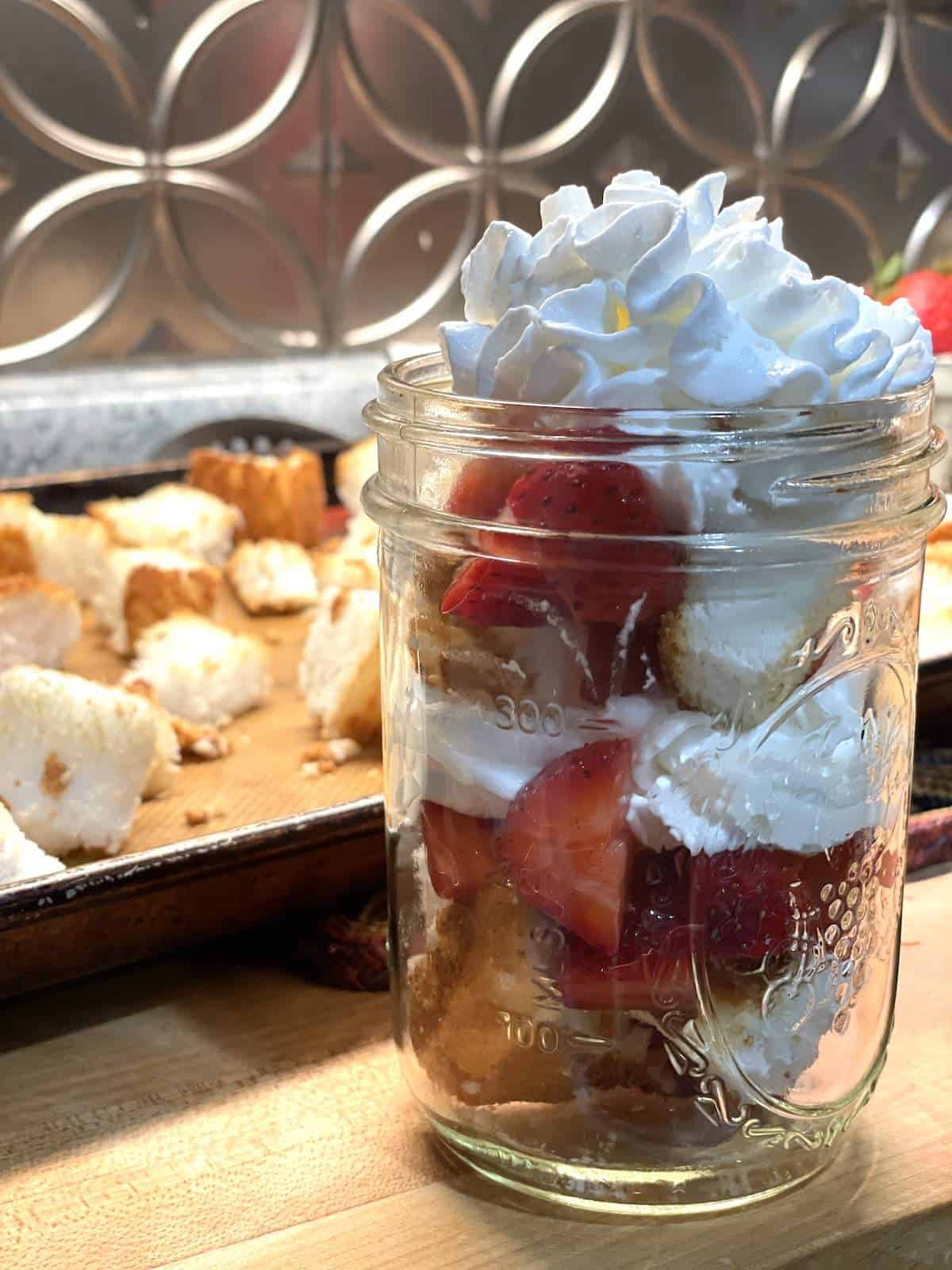 A jar of layers of angel food cake strawberry shortcake in a mason jar.