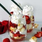 Two angel food cake strawberry shortcakes in stemless wine glasses topped with whipped cream.