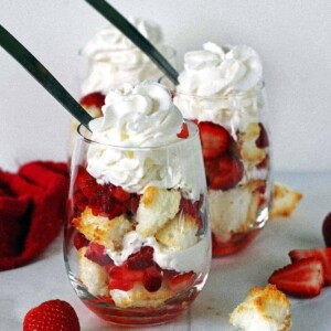Two angel food cake strawberry shortcakes in stemless wine glasses topped with whipped cream.