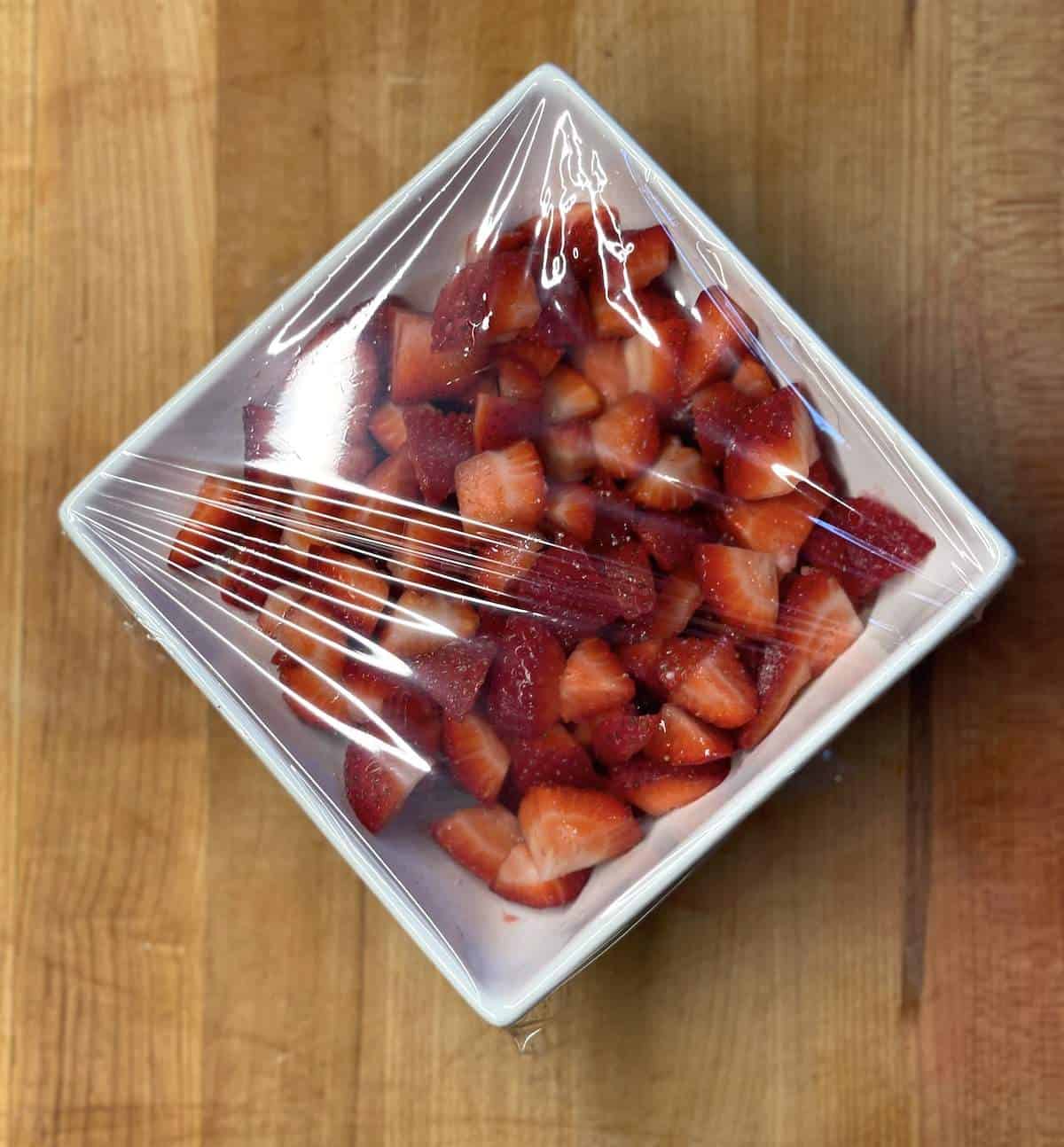 A bowl of sugar coated strawberries wrapped in plastic.