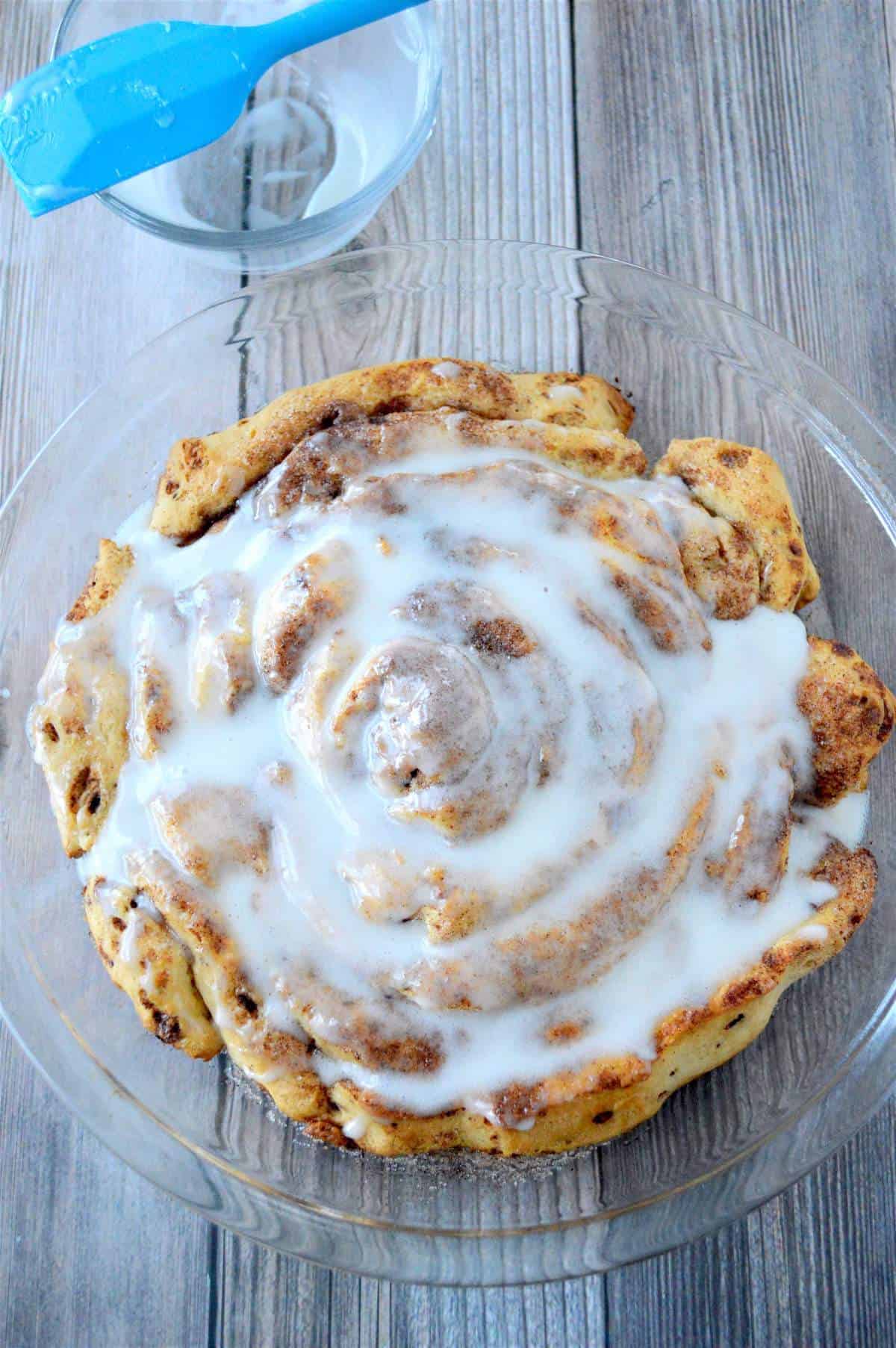 A giant fluffy cinnamon roll covered in cream cheese icing with a spatula on the side.
