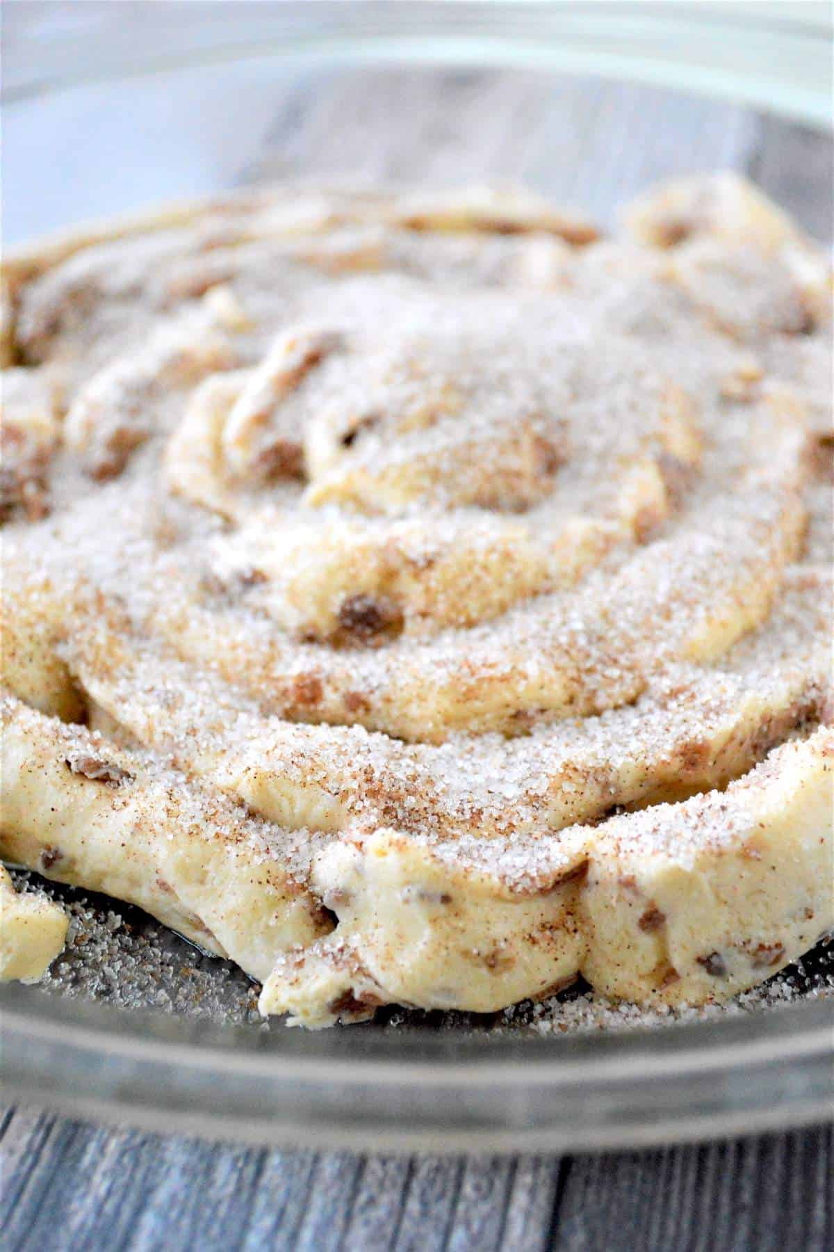 An unbaked giant cinnamon roll in a baking dish covered in cinnamon sugar.