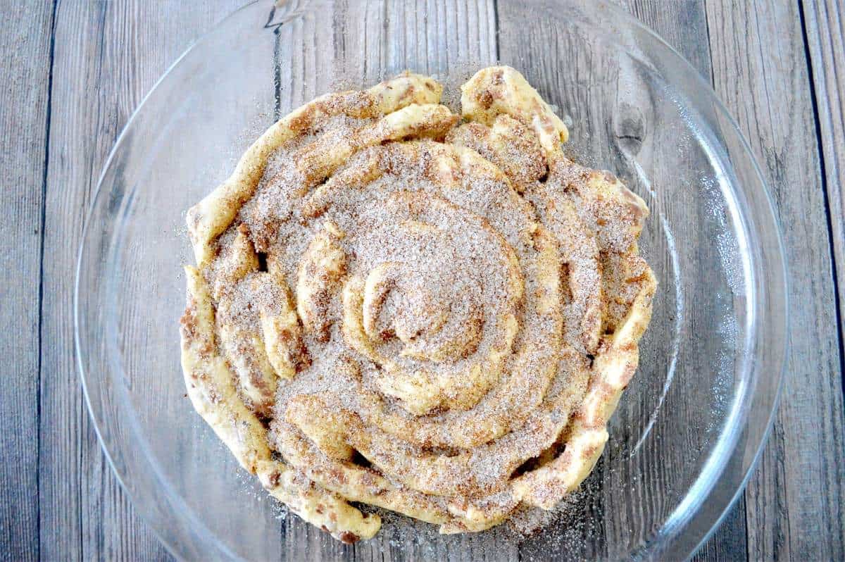 An unbaked giant cinnamon roll covered in cinnamon sugar.