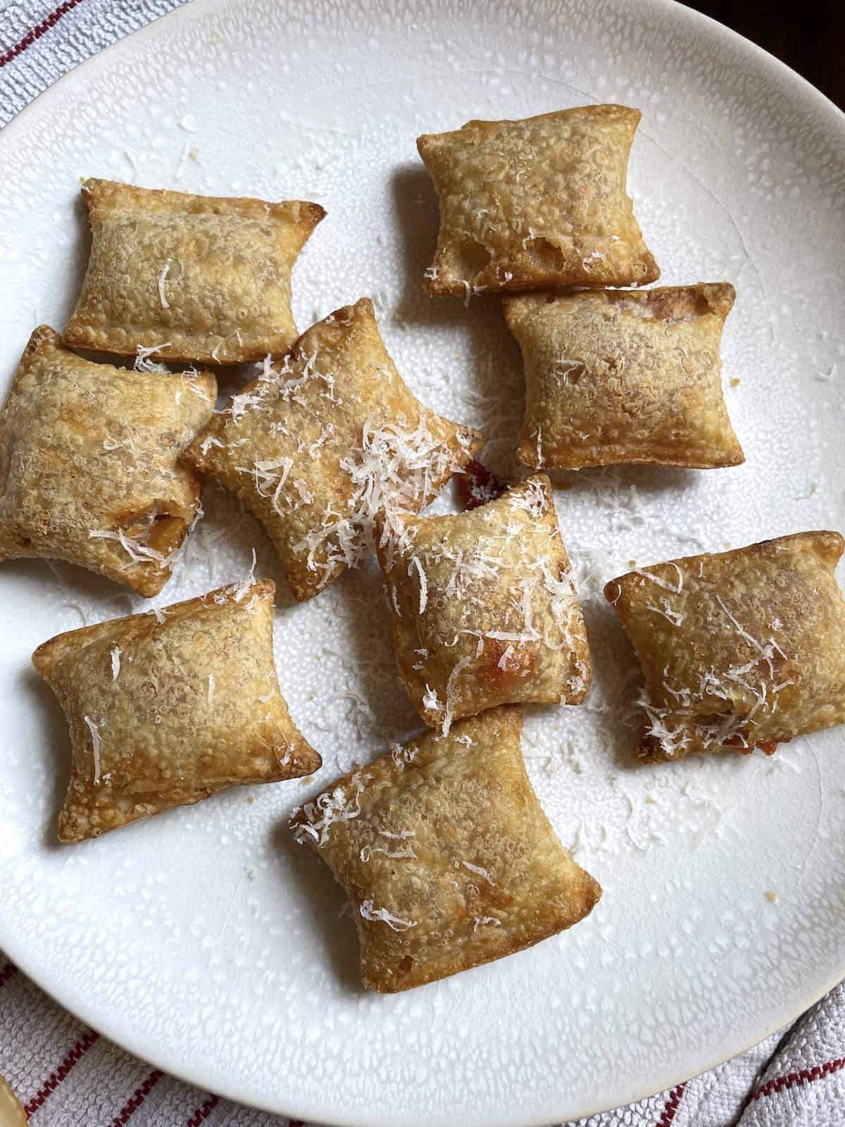 Air fried pizza rolls on a white plate topped with grated parmesan cheese.