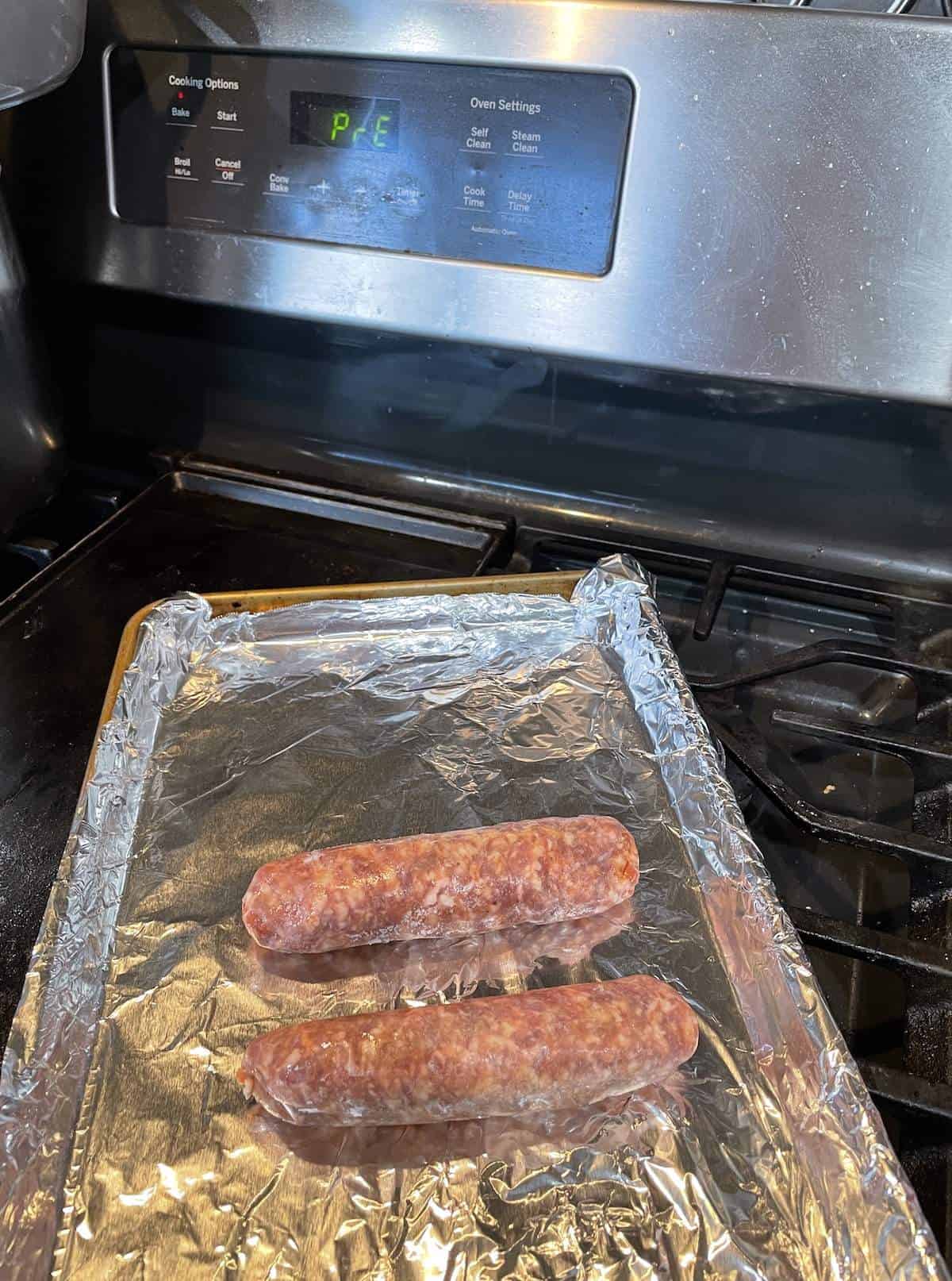 Two uncooked Italian sausages with an oven preheating in the background.
