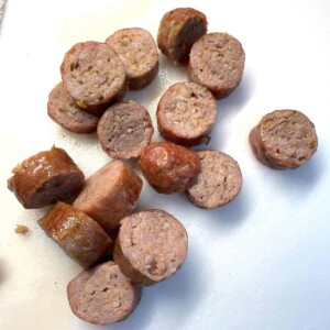 Oven-cooked, sliced Italian sausage on a white cutting board.