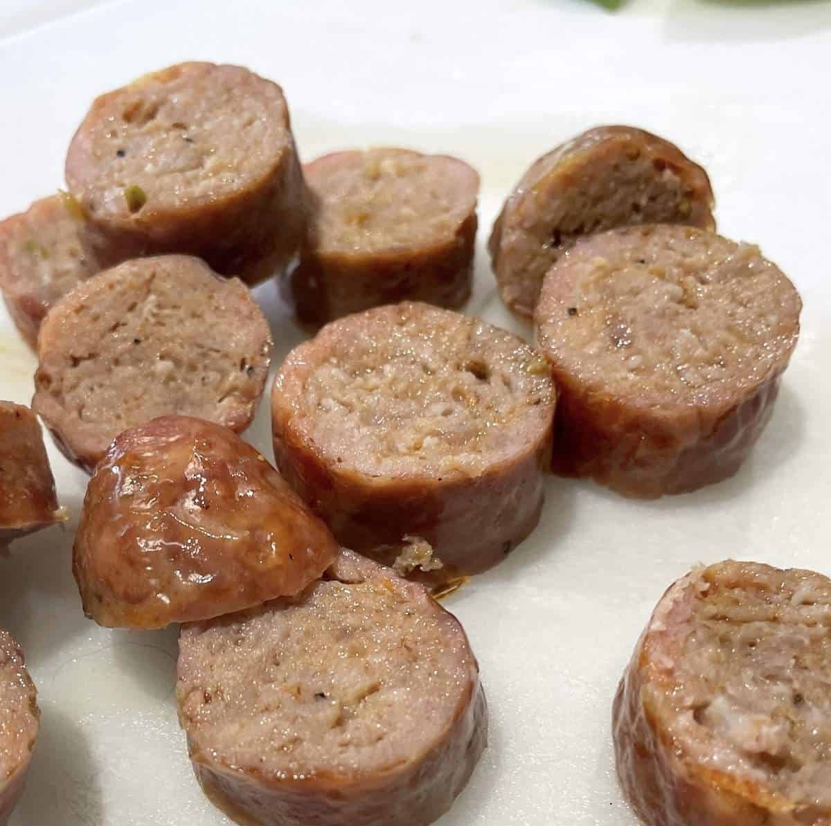 Oven-baked, sliced Italian sausage on a white cutting board.