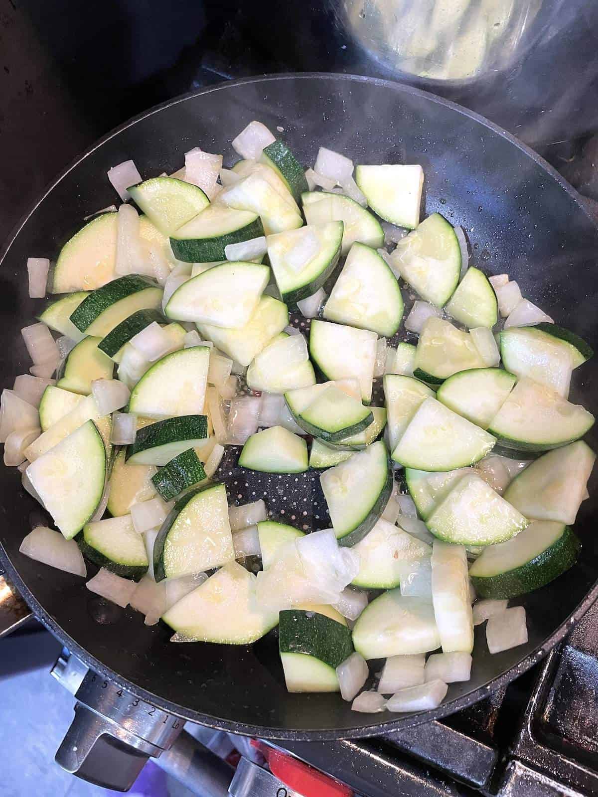 A frying pan with sautéed zucchini and onions cooking in it.