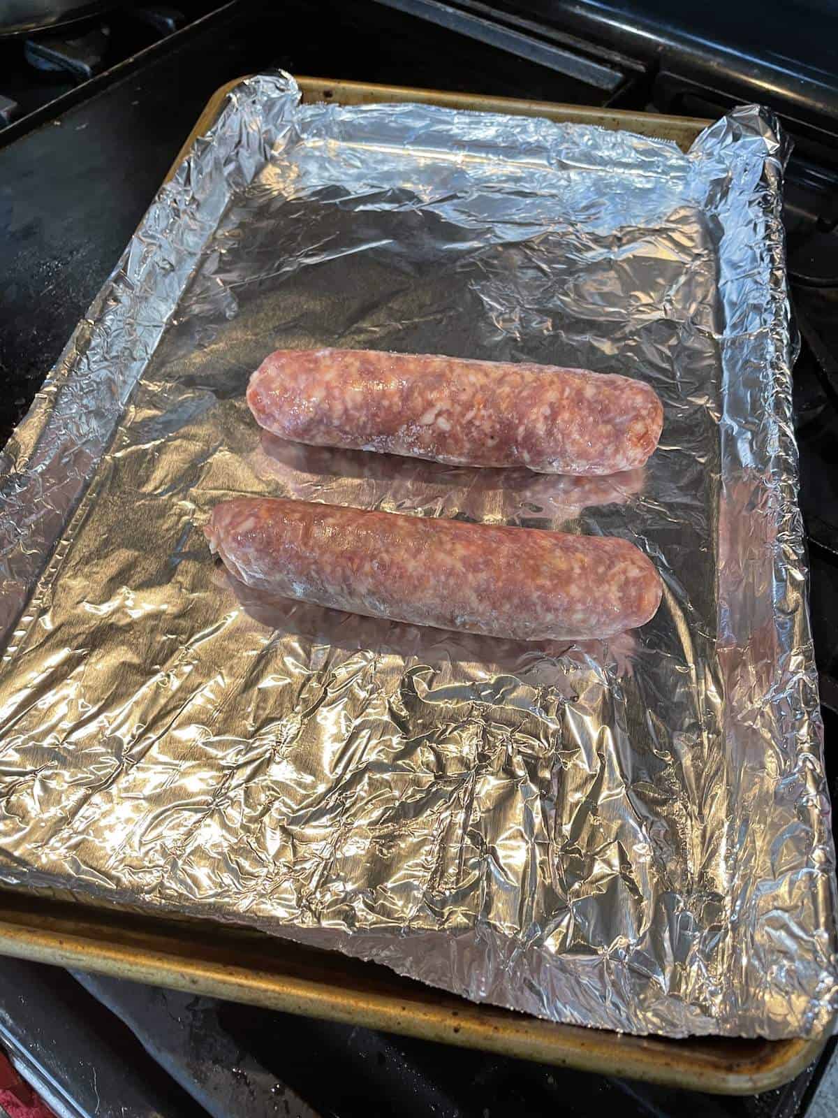 Two uncooked Italian sausage links on a foil lined baking sheet.