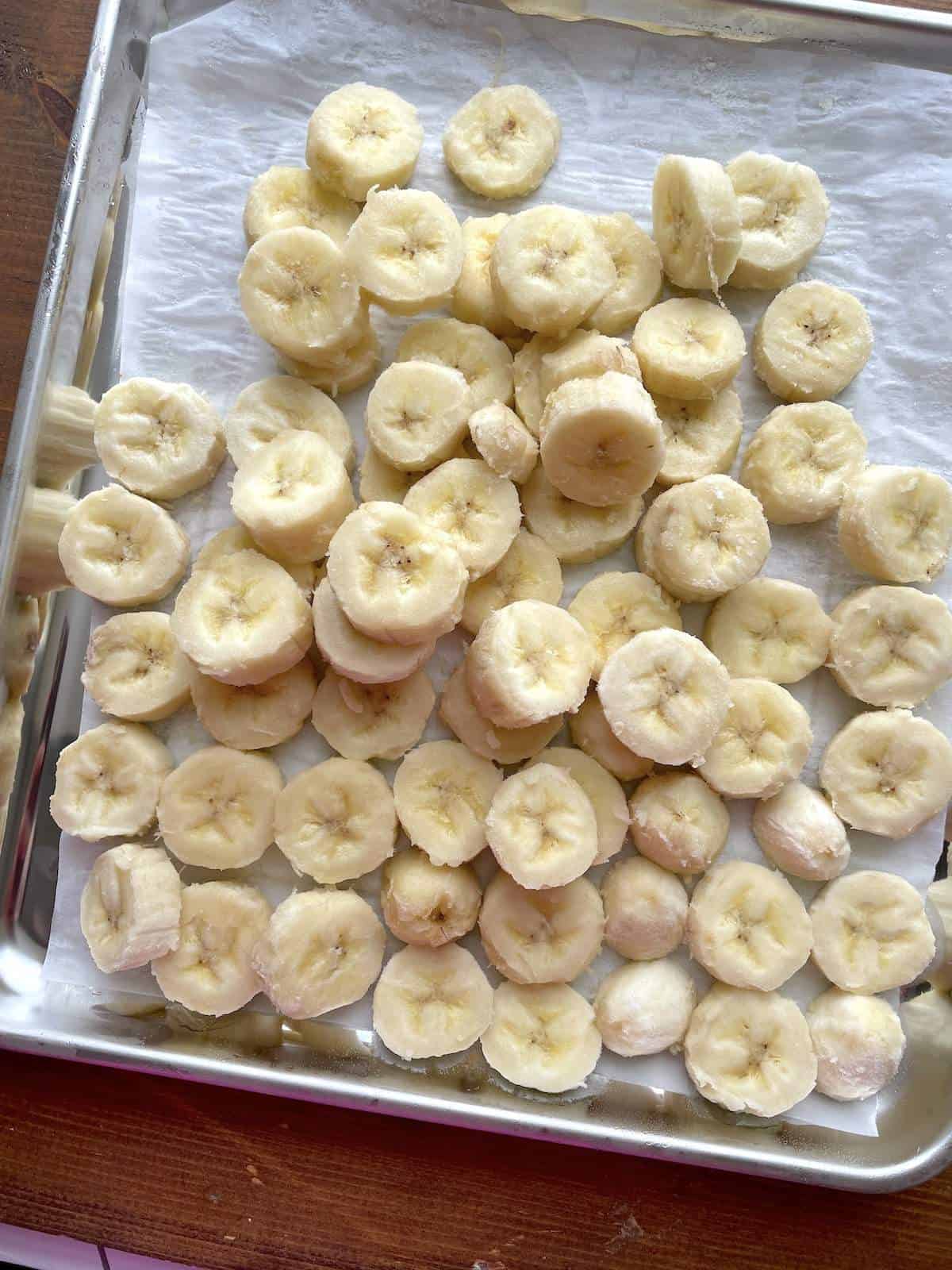 Slices of frozen bananas on a parchment paper lined baking sheet.