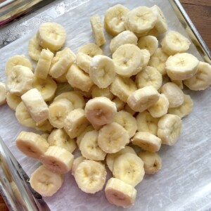 A pile of frozen banana slices on a parchment lined baking sheet.