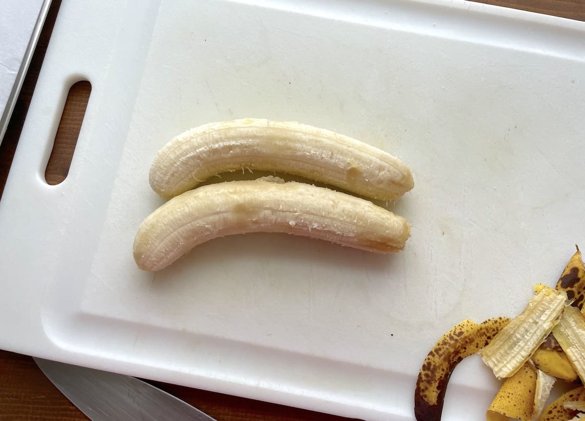 Two ripe bananas on a white cutting board ready to be sliced.